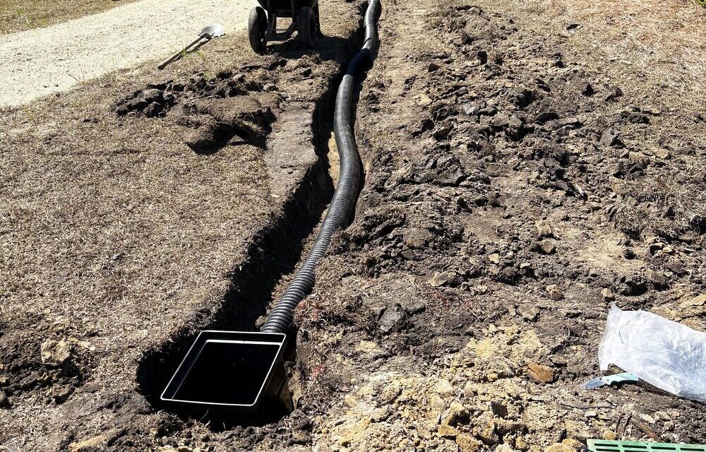 French drain installation with catch basin and corrugated pipe in an open trench